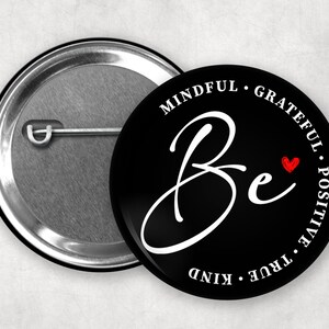 May include: Black button with white text that reads "Be mindful, grateful, positive, true, kind" with a red heart symbol.