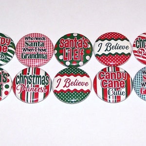 May include: A collection of Christmas-themed buttons with various designs and text. The buttons feature phrases like "Candy Cane Cutie," "Santa's Lil Elf," and "Christmas Princess" in red and green colors.