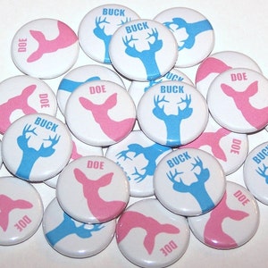 May include: A collection of round, white buttons with blue and pink deer silhouettes. The buttons have the words "BUCK" and "DOE" printed on them.