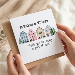 Peut inclure: Carte de vœux avec le texte "It Takes a Village" et "Thank you for being a part of ours." La carte présente des illustrations de maisons colorées. La carte est tenue dans une enveloppe marron.