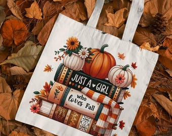 May include: A white tote bag with a fall-themed design. The design includes pumpkins, books, flowers, and the text "JUST A GIRL who loves Fall." The bag has white handles and is surrounded by autumn leaves.