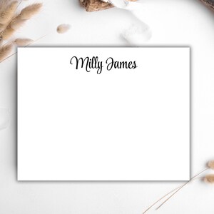 Puede incluir: Una tarjeta de papelería blanca con el nombre "Milly James" en elegante escritura negra. La tarjeta rectangular tiene un diseño limpio y minimalista. El fondo es blanco suave, con acentos florales secos.