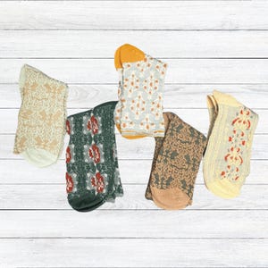 May include: Five pairs of patterned socks in various colors. Designs include floral and geometric patterns in shades of beige, green, orange, and yellow. The socks are displayed on a white wooden surface.