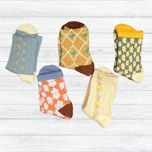 May include: Five pairs of patterned socks in various colors. Designs include floral, butterfly, and geometric patterns. Colors include blue, orange, yellow, green, and cream. The socks are displayed on a white wooden surface.