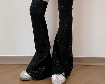 May include: Black, sparkly leg warmers with a flared bottom. The leg warmers are worn over white sneakers with gray soles. The background is a plain white wall and a wooden floor.