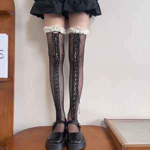 Puede incluir: Medias altas negras de red con un diseño de cordones en la parte delantera. Las medias tienen un ribete de encaje blanco en la parte superior. La persona lleva zapatos negros de plataforma con hebilla.