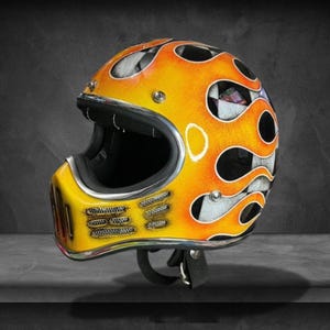 Peut inclure: Casque de moto personnalisé avec un motif de flammes vives en jaune et orange. Le casque présente un motif de drapeau à damier et un intérieur noir. La mentonnière a un motif en maille et une sangle noire.