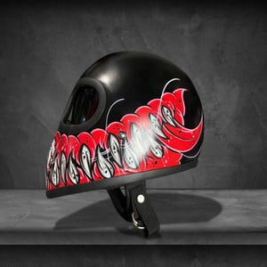 May include: Black motorcycle helmet with a red and white graphic design. The helmet features a rounded visor opening and a chin strap. The graphic design is a stylized, abstract pattern in red and white.