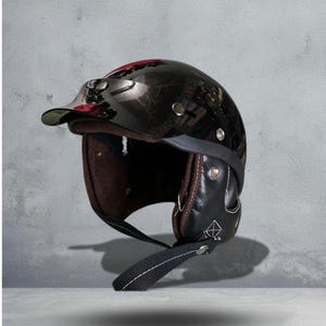 May include: A glossy black motorcycle helmet with a visor. The helmet has a brown interior and black leather ear flaps with white stitching. A black strap with white stitching is attached. The helmet is designed for safety and style.