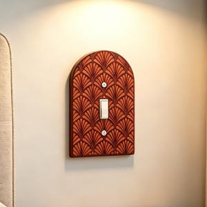 May include: An arched light switch cover plate featuring a repeating fan-shaped pattern in shades of burnt orange and dark brown. The plate is rectangular with a rounded top and includes a single white toggle switch centered with two mounting screws.