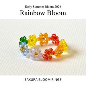 May include: A colourful beaded ring with a floral design. The ring is made up of small, flower-shaped beads in a rainbow of colours, including green, blue, purple, yellow, orange, and red. Text on the image reads "Early Summer Bloom 2026" and "Rainbow Bloom". The text "SAKURA BLOOM RINGS" is also visible.