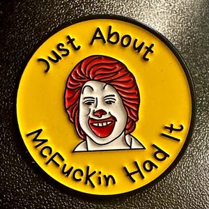 May include: A yellow circular pin with the phrase "Just About McFuckin Had It" in black lettering. The pin features a cartoon illustration of a clown with red hair and a red nose.