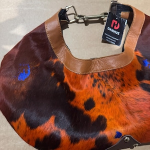 May include: A shoulder bag with a unique pattern of brown, orange, and black fur. The bag has a brown leather trim and a metal chain strap. A tag with the brand name "DANHUZ" is attached.