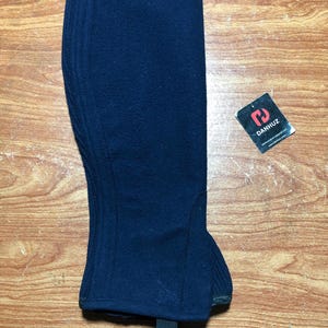 May include: A navy blue riding half chap with a textured surface. The chap has a strap at the bottom and a tag with the brand name "DANHUZ". The chap is designed to protect the lower leg.