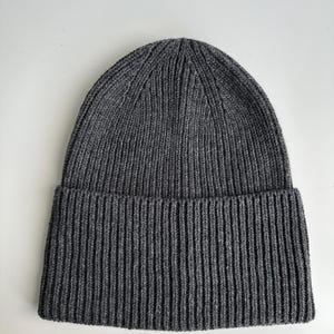 May include: A dark gray ribbed knit beanie hat. The hat has a folded brim and a close-fitting design. The material appears to be a soft, warm knit, suitable for cold weather. The hat is a solid color and has a simple, classic style.