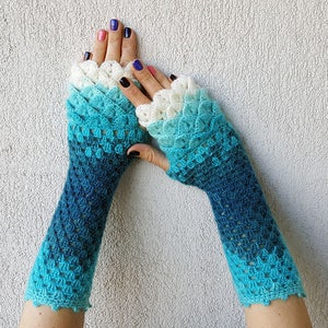 May include: A pair of blue and white crocheted fingerless gloves with a scalloped edge. The gloves are made with a gradient yarn that transitions from white to blue.