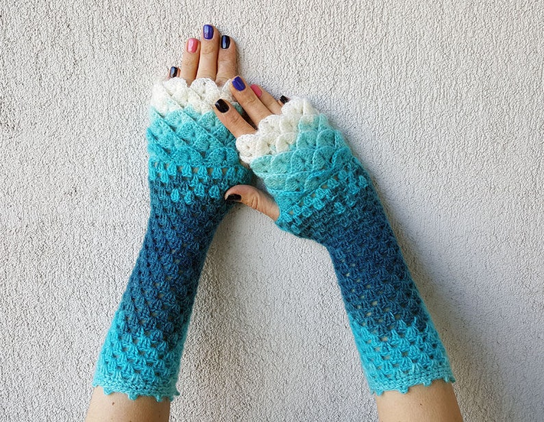 May include: A pair of blue and white crocheted fingerless gloves with a scalloped edge. The gloves are made with a gradient yarn that transitions from white to blue.