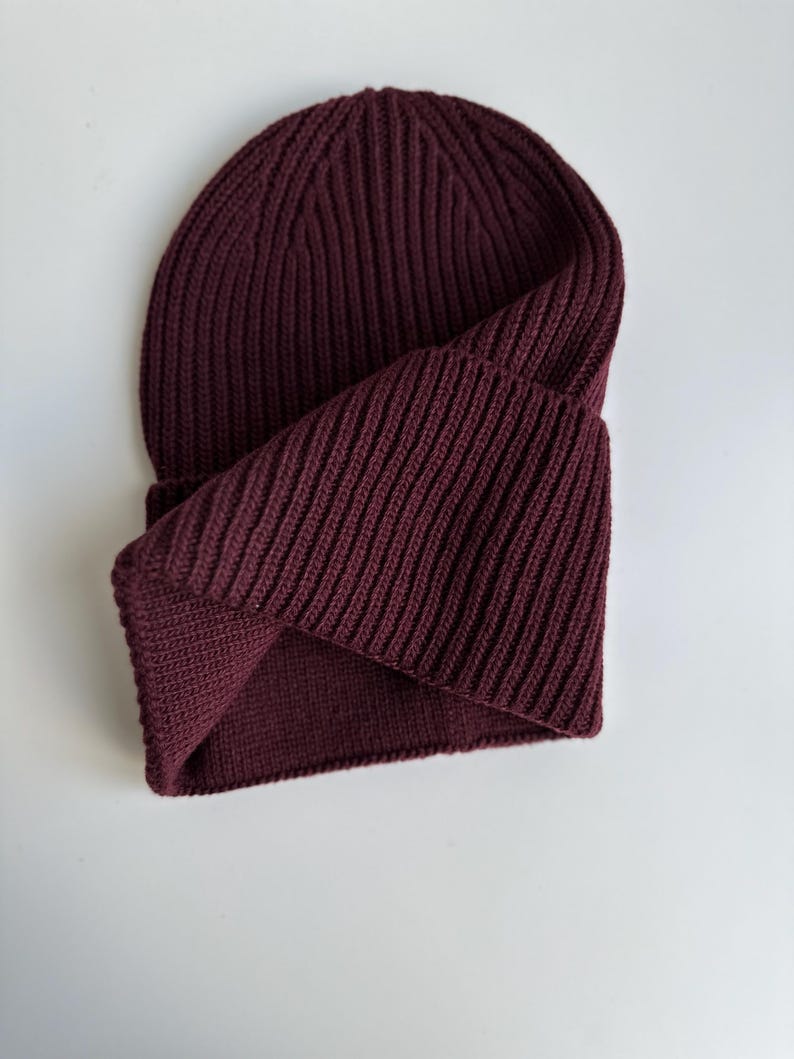 May include: A burgundy ribbed knit beanie hat. The hat is folded over, revealing the interior. The knit pattern runs vertically. The hat is made of a soft, warm material, perfect for cold weather.