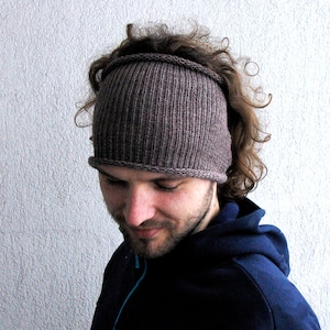 Può includere: Un cerchietto di lana marrone con una trama a coste. Il cerchietto è indossato sulla testa di una persona con i capelli tirati indietro.