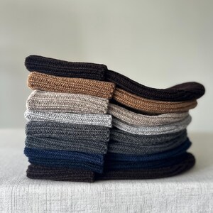May include: A stack of various colored socks, including shades of brown, gray, and navy blue. The socks are neatly folded and stacked on top of each other, showcasing their different hues and textures. The socks appear to be made of a soft, knitted material.