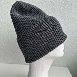 May include: A dark gray ribbed knit beanie hat. The hat is folded at the brim and is displayed on a white mannequin head. The hat is made of a soft, warm material, perfect for cold weather.