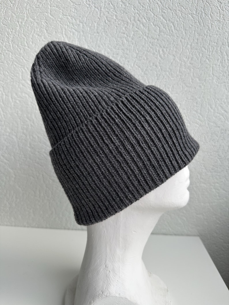 May include: A dark gray ribbed knit beanie hat. The hat is folded at the brim and is displayed on a white mannequin head. The hat is made of a soft, warm material, perfect for cold weather.