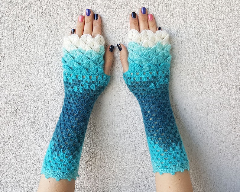 May include: A pair of blue and white crocheted fingerless gloves with a scale pattern. The gloves are ombre, fading from white to blue.