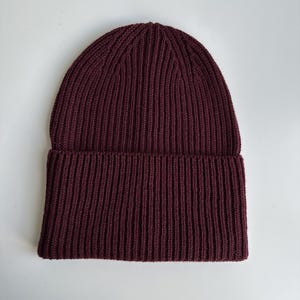 May include: A burgundy ribbed knit beanie hat. The hat is made of a soft, textured material and features a folded brim. The hat is a solid color and is suitable for cold weather.