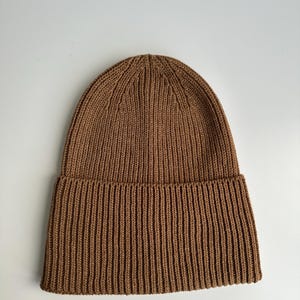 May include: A brown ribbed knit beanie hat. The hat is made of a soft, warm material and features a folded brim. The beanie is a solid color and is suitable for cold weather.