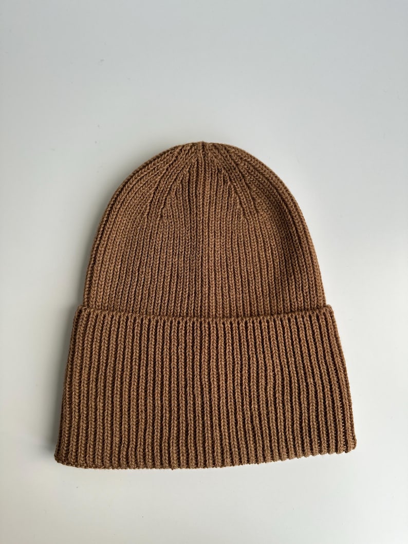 May include: A brown ribbed knit beanie hat. The hat is made of a soft, warm material and features a folded brim. The beanie is a solid color and is suitable for cold weather.