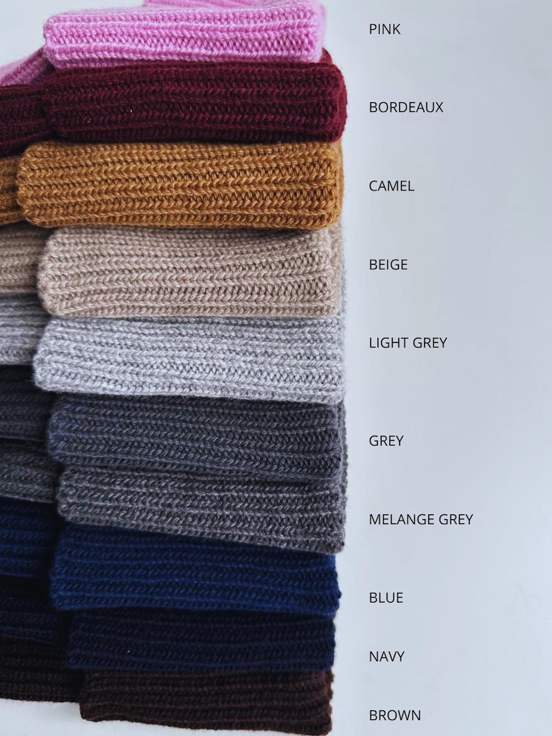 May include: A stack of knitted fabric samples in various colors, including pink, burgundy, camel, beige, light grey, grey, melange grey, blue, navy, and brown. Each sample is labeled with its corresponding color name.