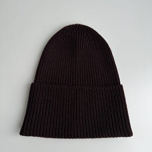 May include: A dark brown ribbed knit beanie hat. The hat has a folded brim and a close-fitting design. The knit pattern runs vertically from the brim to the top of the hat.