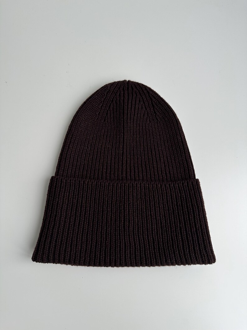 May include: A dark brown ribbed knit beanie hat. The hat has a folded brim and a close-fitting design. The knit pattern runs vertically from the brim to the top of the hat.