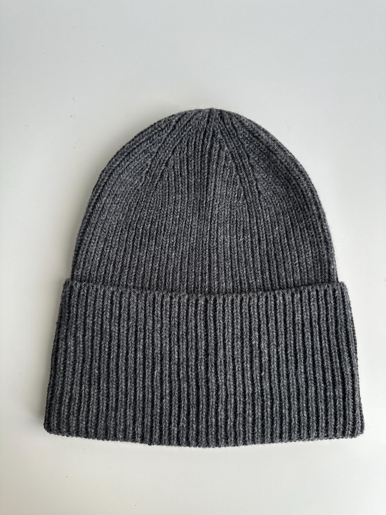 May include: A dark gray ribbed knit beanie hat. The hat has a folded brim and a close-fitting design. The material appears to be a soft, warm knit, suitable for cold weather. The hat is a solid color and has a simple, classic style.