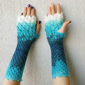 May include: A pair of blue and white crocheted fingerless gloves with a scalloped edge. The gloves are made with a gradient yarn that transitions from white to blue.
