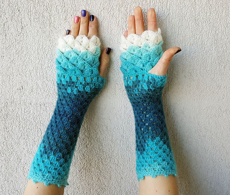 May include: A pair of blue and white crocheted fingerless gloves with a scalloped edge. The gloves are made with a gradient yarn that transitions from white to blue.