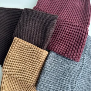 May include: A collection of ribbed knit beanies and matching scarves in various colors. The colors include a deep burgundy, dark brown, tan, and gray. The beanies are folded over at the brim.