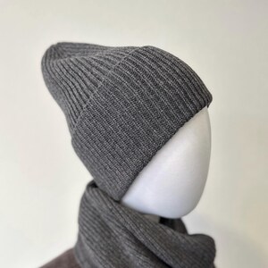 May include: A gray ribbed knit beanie and scarf set. The beanie is a classic style with a folded brim. The scarf is a matching color and texture. The set is displayed on a white mannequin head.