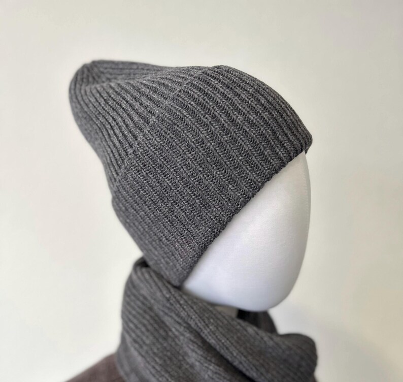 May include: A gray ribbed knit beanie and scarf set. The beanie is a classic style with a folded brim. The scarf is a matching color and texture. The set is displayed on a white mannequin head.
