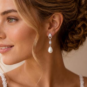 May include: A drop earring featuring a silver-toned setting with a marquise-shaped crystal at the top, a smaller round crystal in the center, and a smooth white teardrop-shaped pearl at the bottom, suspended from a small crystal-encrusted stud.