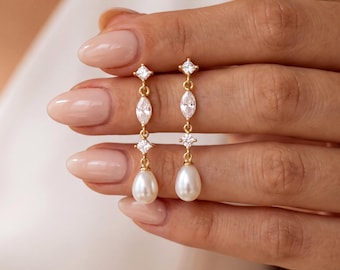 May include: A pair of gold drop earrings featuring a vertical arrangement of a small square-cut clear stone, a marquise-cut clear stone, another square-cut clear stone, and a white teardrop-shaped pearl at the base of each earring.