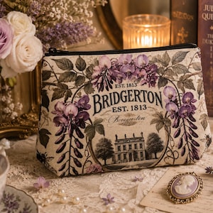 Könnte beinhalten: Eine beigefarbene Stofftasche mit Reißverschluss, bedruckt mit violetten Glyzinienblüten, einem großen Herrenhaus und dem Text "BRIDGERTON EST. 1813". Die Tasche hat einen schwarzen Reißverschluss an der Oberkante und eine trapezförmige Gestalt.