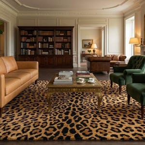 May include: A luxurious living room featuring a tan leather sofa, two green velvet armchairs, and a leopard-print rug. A gold-framed coffee table and a large bookcase add to the elegant decor. The room is well-lit with natural light.