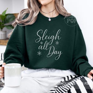 May include: A dark green sweatshirt featuring the text "Sleigh all Day" in white script, with snowflake details. This festive top is a winter holiday garment, perfect for the season.