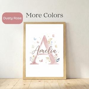 May include: A framed print with a dusty rose letter 'A' and the name 'Amelia' in script. The design incorporates watercolour butterflies and floral elements in pastel shades. The text 'More Colors' is displayed.