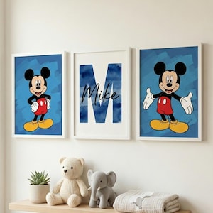 May include: Three framed wall art pieces. Two feature Mickey Mouse on a blue background. The third has a blue watercolor "M" with the name "Mike" in script. A shelf below holds a teddy bear, elephant, plant, and blanket.
