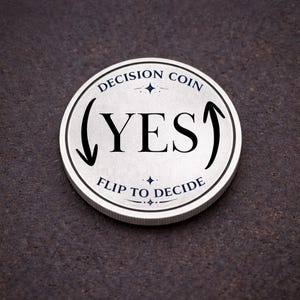 May include: A silver decision coin with the word "YES" in bold black letters. The coin has the text "DECISION COIN" and "FLIP TO DECIDE" in a circular pattern around the edges. Arrows and starbursts are also included in the design.
