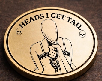 Może przedstawiać: Złota moneta z napisem "HEADS I GET TAIL" w okrągłym wzorze. Moneta przedstawia czarno-białą ilustrację osoby trzymającej włosy, z czaszką po każdej stronie tekstu. Moneta ma podniesioną krawędź.