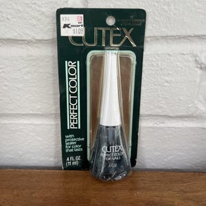 May include: A bottle of Cutex Perfect Color nail polish in a dark shade, with a white cap, displayed on its original packaging. The packaging is dark green with gold accents and the text "Perfect Color" is visible. The bottle contains 11 ml.