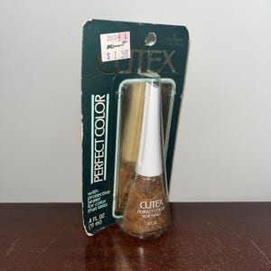 Może przedstawiać: Butelka lakieru do paznokci Cutex Perfect Color w złotym odcieniu, z białą nakrętką. Opakowanie zawiera napis "Perfect Color" i "4 fl oz (11 ml)." Etykieta głosi również "Gold Fever Special Effect."
